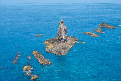 Rock spire rising from coastal rocks in clear blue water at Cape Kamui, Hokkaido, Japan.