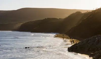 Golden evening light illuminating the rugged coastline near Robin Hood's Bay, with waves breaking along the beach beneath shadowed cliffs.