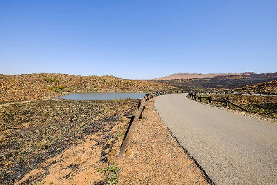 Reserve road winding past a small dam and rocky grassland hills in Suikerbosrand Nature Reserve, Gauteng.
