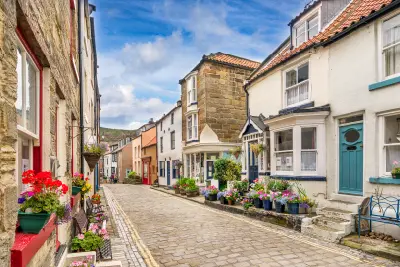 Cobbled high street in Staithes, North Yorkshire, lined with traditional stone cottages, colourful doors, hanging flower baskets and village shops.