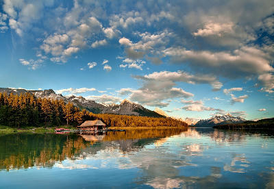 Maligne Lake at sunset with boathouse, golden-lit forest, and mountain reflections on calm water
