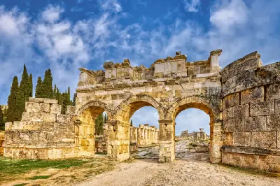 Three-arched Roman gateway opening onto a stone-paved colonnaded street in the ancient city of Hierapolis beneath a dramatic blue sky.