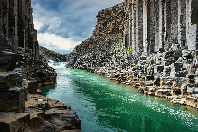 Basalt columns rising above the turquoise river in Stuðlagil Canyon, Eastfjords, eastern Iceland.