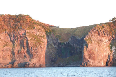 Coastal cliffs with a thin waterfall descending directly into the sea at Furepe Falls, Shiretoko Peninsula, Hokkaido, Japan during autumn evening light.