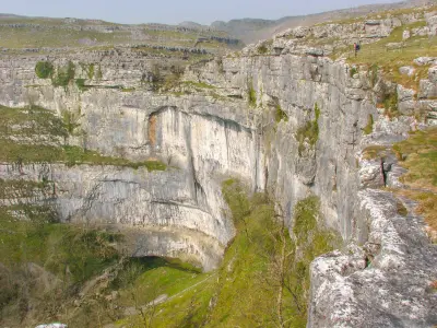 Elevated view of the horseshoe-shaped limestone cliffs of Malham Cove, with rocky ledges and grassy slopes in the Yorkshire Dales, England.