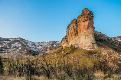 Tall sandstone rock pillar known as Titanic Rock standing against mountain slopes in Golden Gate Highlands National Park, with dry grassland and patches of snow on the surrounding highlands.