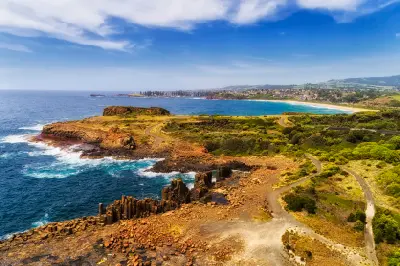 Aerial view across the basalt columns and rugged shoreline of Bombo Headland, with the Pacific Ocean, Bombo Beach and Kiama coastline beyond.