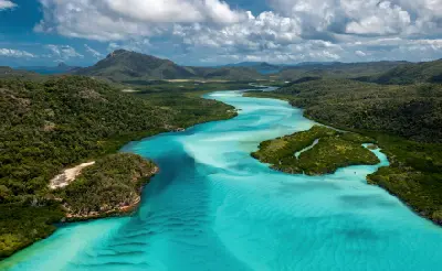 Turquoise water flows through Hill Inlet on Whitsunday Island, revealing shifting sandbanks and rippled shallows between densely forested hills.