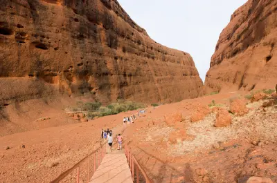 Walkers on the Walpa Gorge trail between towering red sandstone walls at Kata Tjuta in Central Australia.