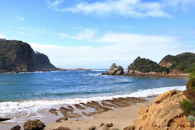 View across the Knysna Lagoon entrance from Featherbed Nature Reserve, showing rocky headlands, sandy shoreline and the Indian Ocean on South Africa’s Garden Route.