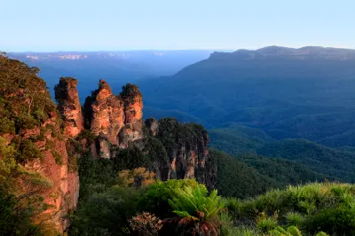 Warm morning light illuminates the Three Sisters sandstone pillars above the forested Jamison Valley in the Blue Mountains.
