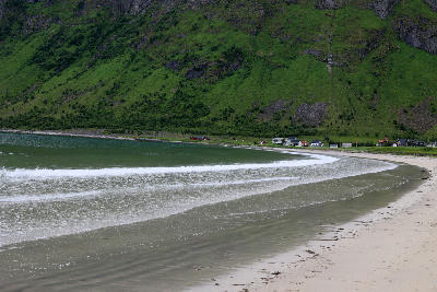 White sand beach at Ersfjord with gentle waves, green mountainside, and scattered houses along the fjord shoreline