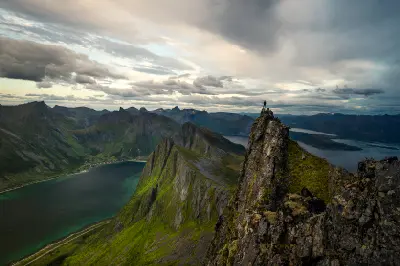 Hiker standing on rocky ridge at Hesten viewpoint Senja Norway overlooking Segla peak and Mefjorden fjord with steep cliffs and layered mountains.
