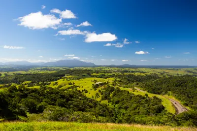 Panoramic view of green farmland, rainforest, winding road and distant mountains near Millaa Millaa in the Atherton Tablelands, Queensland.