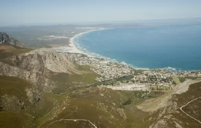 High aerial panorama of Hermanus in South Africa showing Walker Bay, mountain ridges, coastal cliffs, and the long white sand beaches of the Whale Coast in the Western Cape.