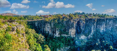 Suspension bridge and cliff-edge visitor facilities spanning Graskop Gorge above a dense indigenous forest in Mpumalanga, South Africa.
