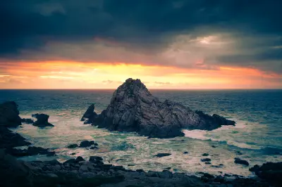 Sugarloaf Rock surrounded by breaking waves beneath a dramatic orange sunset and dark storm clouds in Western Australia’s Margaret River region.