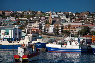 Fishing boats in Mossel Bay Harbour with the coastal town, church spire and hillside neighbourhoods in the background, Western Cape, South Africa.