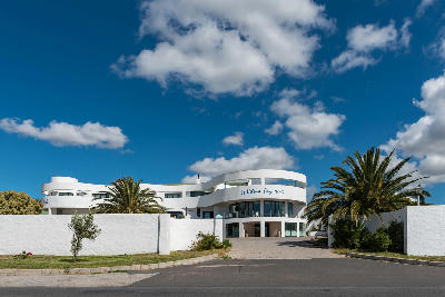 Modern white hotel building in St Helena Bay framed by palm trees and a wide blue sky with scattered clouds on South Africa’s Atlantic coastline.