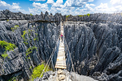 Hiker crossing a suspension bridge above the limestone pinnacles of Tsingy de Bemaraha in Madagascar