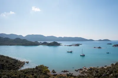 Panoramic view over Kekova, Turkey, with turquoise Mediterranean water, small rocky islands, forested hills and a sailing boat, seen from the Lycian Way hiking trail.