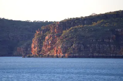 Warm sunrise light illuminates rugged sandstone cliffs above the calm waters of the Hunter River.