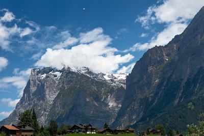 Grindelwald village chalets beneath steep alpine cliffs and cloud-covered peaks in the Bernese Alps, Switzerland.