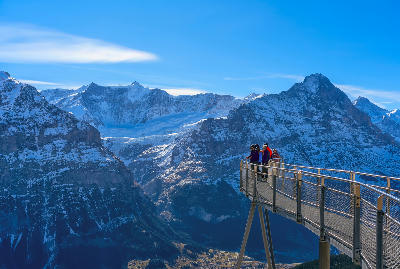 Tourists standing on the First Cliff Walk viewing platform overlooking snow-covered peaks and the valley below in Grindelwald, Switzerland.
