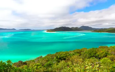 Elevated view across turquoise water, white sandbanks and forested hills at Hill Inlet, Whitsunday Island, Queensland.