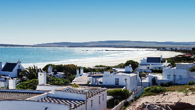 View across whitewashed houses to Paternoster Bay, showing a broad sandy beach, turquoise Atlantic waters and the scenic coastline of South Africa’s West Coast.