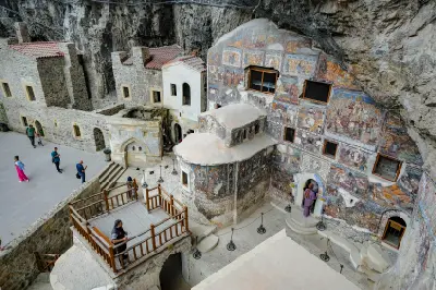 Visitors beside the historic fresco-covered rock church and stone buildings inside Sümela Monastery, Trabzon, Turkey.