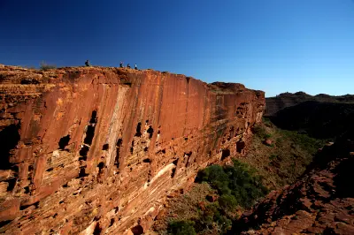 Hikers appear tiny atop the immense red sandstone cliffs of Kings Canyon, highlighting the scale of the canyon along the Rim Walk.