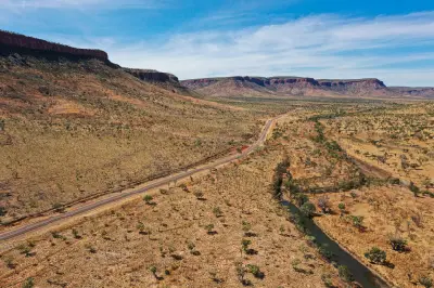 Aerial view of a remote road and river winding beneath rugged sandstone escarpments across the East Kimberley landscape.