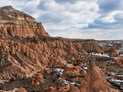 Pink volcanic ridges and layered cliffs in Rose Valley, Cappadocia, Turkey, with patches of melting snow beneath a cloudy sky.
