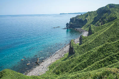 Green coastal cliffs above clear blue water and rocky shoreline at Cape Kamui, Hokkaido, Japan.