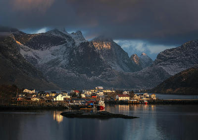 Reine fishing village with boats in the harbour and snow-dusted mountains rising behind in the Lofoten Islands, Norway.