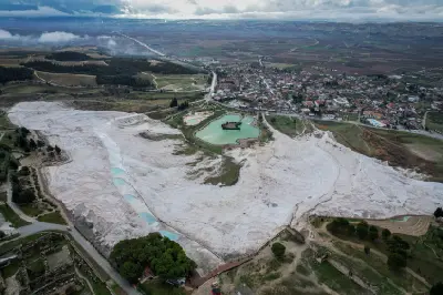 Aerial view of Pamukkale, Turkey, showing the white travertine terraces, turquoise pools, nearby Hierapolis ruins and the town and countryside beyond.