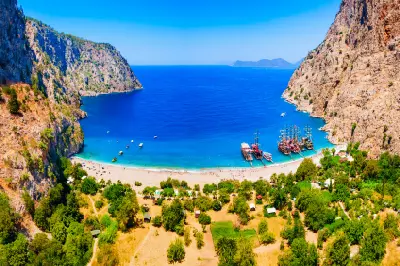 Aerial view of Butterfly Valley with its beach, turquoise Mediterranean waters, steep cliffs and boats near Ölüdeniz, Türkiye.
