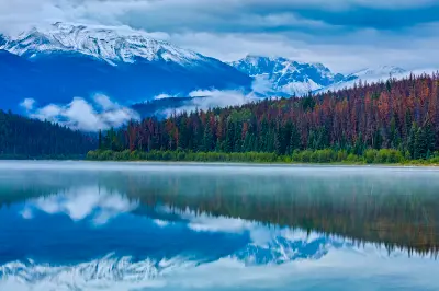 Patricia Lake with storm clouds, mist, and snow-covered mountains reflected in calm water