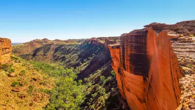 Towering red sandstone cliff above the vegetated gorge of Kings Canyon in Watarrka National Park, Northern Territory, Australia.