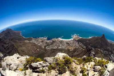 High vantage panorama overlooking Clifton Beaches and the Atlantic Ocean, with mountain slopes and rocky foreground above Cape Town’s Atlantic coastline.