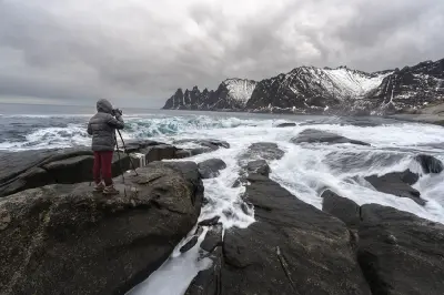Photographer standing on Tungeneset rocks with waves and Okshornan mountains in background, Senja