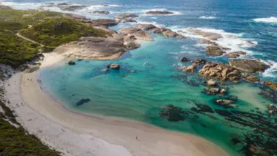 Aerial shot looking down at the white sandy shoreline, emerald waters, and scattered rock formations of Greens Pool.