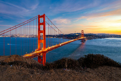 Golden Gate Bridge at sunset with San Francisco skyline and glowing lights reflecting across the bay