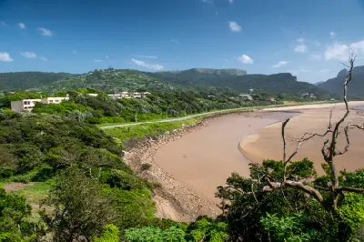 View over the Mzimvubu River estuary at Port St Johns on the Wild Coast of the Eastern Cape, South Africa, with forested hills, sandy riverbanks and coastal vegetation surrounding the river mouth.