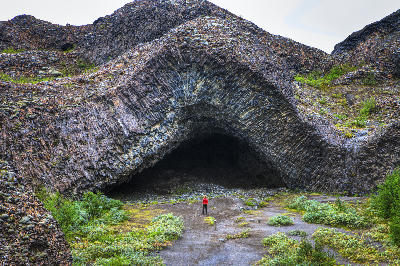 Woman standing beneath the basalt cave formations of Hljóðaklettar in North Iceland, showing curved and angled volcanic columns shaped by the Jökulsá River.