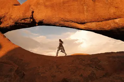 Woman walking beneath a natural granite arch at Spitzkoppe in Namibia during warm sunset light.