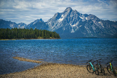 Mount Moran reflected across Jackson Lake with forested shoreline and rocky beach in Grand Teton National Park, Wyoming, USA.