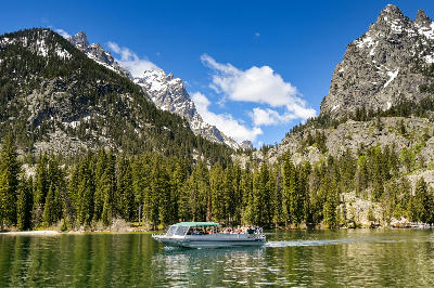 Boat crossing Jenny Lake with forested shoreline and mountain peaks rising behind, Grand Teton National Park, Wyoming, USA.