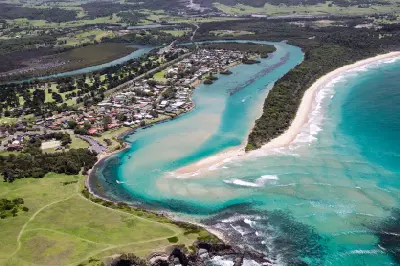 Aerial view of the turquoise Minnamurra River estuary winding past the coastal settlement and sandbar before meeting the Pacific Ocean.